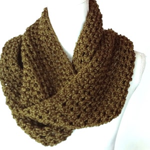 May include: A handmade, olive green infinity scarf. The scarf is made of a chunky, textured yarn, and is displayed on a white mannequin. The knitted loop scarf is a warm accessory for cold weather. The color is a muted, earthy tone.