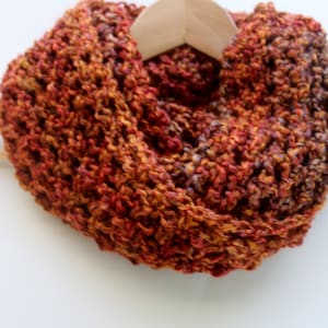 May include: A chunky knit scarf in shades of orange, brown, and red. The scarf is displayed on a wooden hanger.