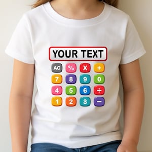 May include: White t-shirt featuring a colorful calculator design. The design includes a red-bordered rectangle with the text "YOUR TEXT" above a grid of calculator buttons with numbers and symbols. The child is wearing blue jeans.