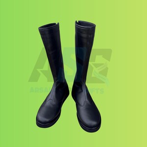May include: A pair of black knee-high boots. The boots are made of a smooth, matte material and have a streamlined design. The boots are set against a green gradient background. The boots are a classic style.