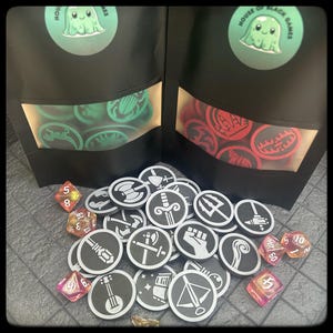 Könnte beinhalten: Ein Satz von 18 schwarzen und weißen runden Spielsteinen mit verschiedenen Symbolen, darunter ein Schwert, eine Faust, ein Dreizack, eine Welle, eine Laute und ein Stern. Die Spielsteine liegen auf einer grauen Oberfläche mit roten und weißen Würfeln.