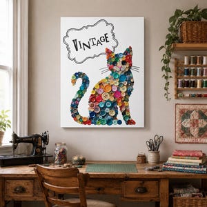 May include: A canvas art piece featuring a cat silhouette crafted from colorful buttons. The word "VINTAGE" is written above the cat in a black, decorative font. The artwork is displayed in a craft room setting, with a sewing machine and wooden desk.