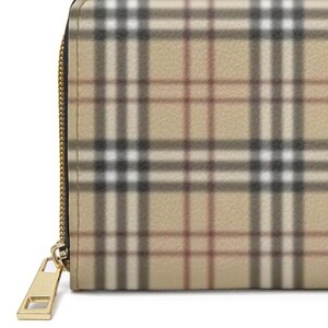 May include: Close-up of a beige wallet with a classic plaid pattern in black, white, and brown. The wallet has a gold-colored zipper and pull. The design is a timeless accessory.