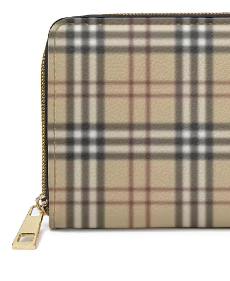 May include: Close-up of a beige wallet with a classic plaid pattern in black, white, and brown. The wallet has a gold-colored zipper and pull. The design is a timeless accessory.