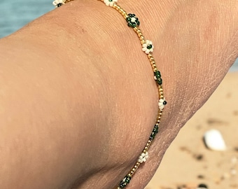 May include: A gold beaded bracelet with white and green flower accents.