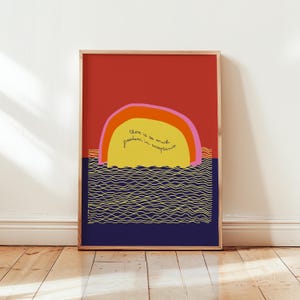 Könnte beinhalten: Gerahmter Kunstdruck mit einem Sonnenuntergangsdesign. Der Himmel ist rot, die Sonne gelb und das Wasser blau. Die Sonne trägt den Text "there is so much freedom in acceptance". Das Kunstwerk ist in einem Holzrahmen.