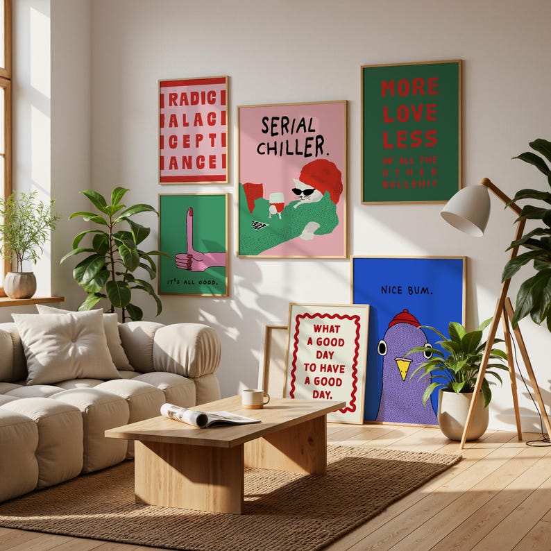 May include: A living room scene featuring several framed art prints with bold text and illustrations. The prints have various colors, including pink, green, and blue. A wooden coffee table and a beige sofa are in the foreground.