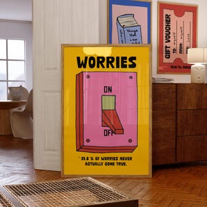 Op de afbeelding: Een ingelijste gele poster met het woord "WORRIES" boven een roze lichtschakelaar illustratie. De schakelaar staat in de "OFF" positie. De tekst onderaan luidt "99,8% VAN DE ZORGEN KOMEN NOOIT ECHT UIT."