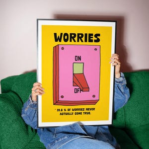 K&ouml;nnte beinhalten: Ein gerahmtes Poster mit gelbem Hintergrund und dem Wort "WORRIES" in Schwarz. Ein rosa Schalter mit "ON" und "OFF" befindet sich in der Mitte. Der Text "99,8% OF WORRIES NEVER ACTUALLY COME TRUE" steht unten.