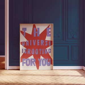 Pode incluir: Um p&ocirc;ster com uma estrela vermelha e texto azul que diz "THE UNIVERSE IS ROOTING FOR YOU".