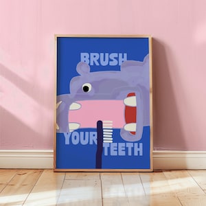 Könnte beinhalten: Ein gerahmter Kunstdruck mit einem lila Nilpferd, das sich die Zähne mit einer rosa Zahnbürste putzt. Die Worte "BRUSH YOUR TEETH" stehen in blauer Schrift auf blauem Hintergrund. Das Kunstwerk wird auf einem Holzboden präsentiert.