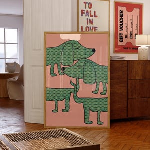 May include: A framed vertical wall art print featuring three stylized green dogs with dark green dotted patterns on a solid pink background. The dogs have closed eyes and simple outlines, arranged in a stacked composition within a light wood frame.
