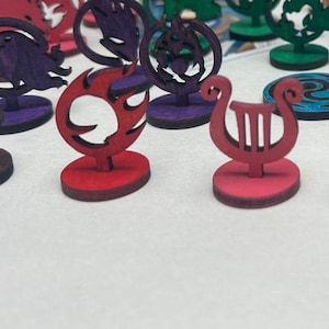 May include: A set of 18 wooden game pieces with various symbols and designs. The pieces are painted in different colors, including red, blue, green, purple, and brown. Each piece has a small base.