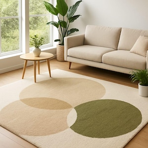 Op de afbeelding: Crèmekleurig vloerkleed met overlappende cirkels in beige en olijfgroen. Het kleed ligt in een woonkamer met een beige bank, een kleine houten bijzettafel en een groot raam. Afmetingen: ongeveer 200 cm x 300 cm.