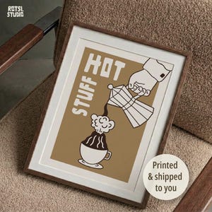May include: A framed wall art print featuring a tan background with a white graphic illustration of a hand pouring coffee from a moka pot into a cup. The text STUFF HOT is printed in white block letters. The frame is made of dark brown wood.