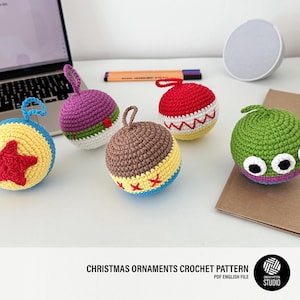 Puede incluir: Cinco adornos navideños de ganchillo en diferentes colores y diseños. Los adornos tienen forma de bola y presentan varios patrones, incluyendo estrellas, rayas y ojos.