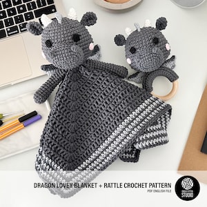 May include: Two grey crochet dragon lovey blankets and a rattle. The larger blanket has a dragon head and arms attached to a square blanket. The smaller dragon has a wooden ring. The text "DRAGON LOVEY BLANKET + RATTLE CROCHET PATTERN" is visible.