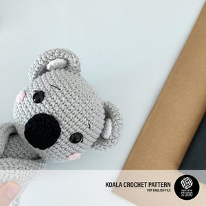 Puede incluir: Un juguete de koala tejido a ganchillo en color gris con una nariz negra grande, ojos de seguridad negros y mejillas rosadas pequeñas. El koala tiene orejas redondeadas con detalles blancos. El texto dice KOALA CROCHET PATTERN PDF ENGLISH FILE.