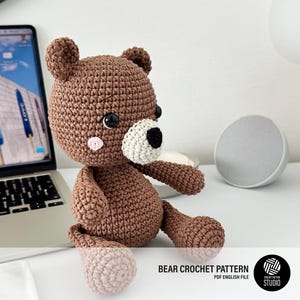 Puede incluir: Un oso de ganchillo marrón con un hocico color crema, una nariz negra y pequeñas mejillas rosadas. El oso tiene grandes ojos negros y está hecho con un punto de lana texturizado. El texto en la imagen dice: BEAR CROCHET PATTERN PDF ENGLISH FILE.