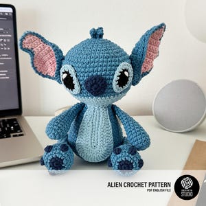 Puede incluir: Muñeco alienígena de ganchillo azul con orejas grandes, ojos negros y nariz azul oscuro. El muñeco está sobre una superficie blanca. El texto "ALIEN CROCHET PATTERN PDF ENGLISH FILE" es visible.