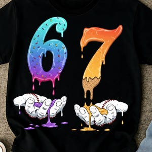 May include: Black t-shirt featuring the number 67 in a dripping, colorful design. The number 6 is blue to purple with sprinkles, and the 7 is orange to yellow with a waffle cone base. Baseball hands hold the dripping numbers.