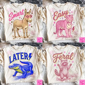 Puede incluir: Cuatro camisetas color crema con gráficos de animales y texto. Una camiseta presenta un burro con gafas de sol con la palabra "Smart". Otra muestra un tigre rosa con la palabra "Easy". Una tercera muestra un caimán azul con "Later". La última tiene un mapache con "Feral".