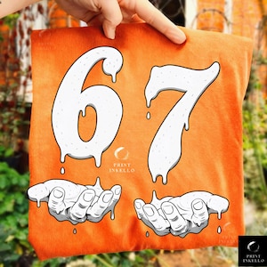 May include: Orange t-shirt with the number "67" in a dripping white font. Below the numbers are two hands with dripping white paint. The Print Inkello logo is at the bottom.