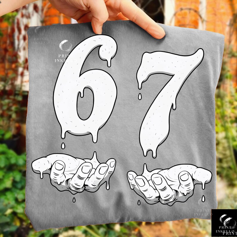 May include: A gray t-shirt featuring the numbers "67" in a dripping, textured white font. Below the numbers are two hands, also in white, with a dripping effect. The shirt has the "Print Ink Print" logo in the upper left and lower right corners.