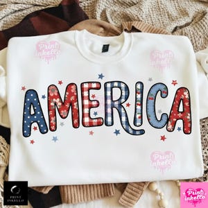 May include: White sweatshirt featuring the word "AMERICA" in patterned letters. The letters are decorated with floral, polka dot, and gingham patterns in red, white, and blue. Small red and blue stars are scattered around the word.