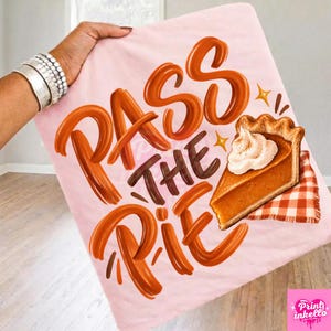Puede incluir: Un artículo de tela rosa claro con el texto naranja PASS THE PIE en una fuente de estilo pincel. A la derecha del texto hay un gráfico de una porción de pastel de calabaza con crema batida, sobre una servilleta de cuadros rojos y blancos.