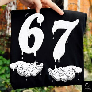 Puede incluir: Camiseta negra con el número "67" en fuente blanca goteante. Debajo, dos manos blancas con líquido goteando. La camiseta tiene el logo "Print Inkello" en la esquina inferior derecha.