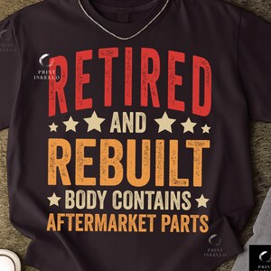 May include: Dark brown t-shirt with the text "RETIRED AND REBUILT BODY CONTAINS AFTERMARKET PARTS" in red and orange. The design includes star accents. A silver chain is visible at the top.