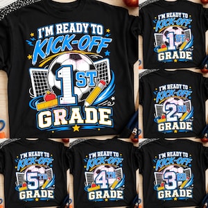 Può includere: Una t-shirt nera con una stampa grafica raffigurante un pallone da calcio, una rete da porta, una matita gialla e una mela rossa. Il testo recita I'M READY TO KICK-OFF seguito dal livello scolastico in grandi numeri blu e bianchi.
