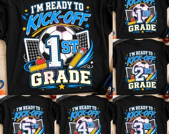 May include: A black t-shirt featuring a graphic print with a soccer ball, a goal net, a yellow pencil, and a red apple. The text reads I'M READY TO KICK-OFF followed by the grade level in large blue and white numbers and the word GRADE.
