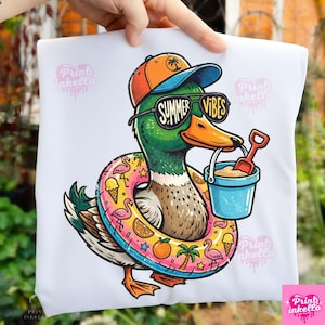 May include: White t-shirt featuring a cartoon duck wearing sunglasses with the text "Summer Vibes." The duck is wearing a hat and a colorful inflatable ring. It holds a bucket and shovel, suggesting a beach theme.