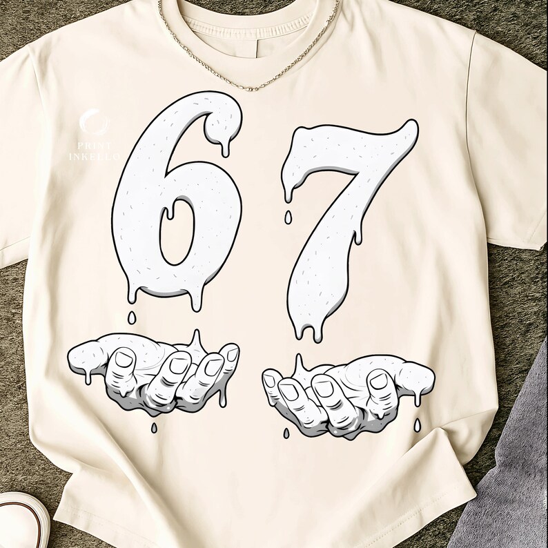 May include: Cream-colored t-shirt featuring a graphic design. The design includes the numbers "67" in a dripping style, with each number above a pair of hands. The hands are cupped, with drips falling from the numbers into the hands. A silver chain is around the neck.
