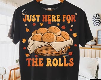 May include: Black t-shirt with the text "JUST HERE FOR THE ROLLS" in orange and yellow. The shirt features a graphic of a basket filled with rolls, surrounded by autumn leaves.