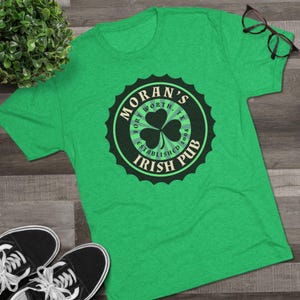 May include: Green t-shirt with a black and white circular logo that says "Moran's Irish Pub" with a shamrock inside. The logo also says "Fort Worth, TX Established 2004".