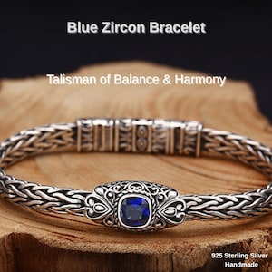 Könnte beinhalten: Ein silbernes Armband mit einem geflochtenen Kettenmuster und einem zentralen blauen Zirkonstein. Das Armband ist mit "Blue Zircon Bracelet" und "Talisman of Balance & Harmony" beschriftet. Der Text "925 Sterling Silver Handmade" ist ebenfalls sichtbar.