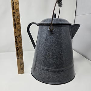 May include: A gray enamelware pitcher with a wooden handle and a wire bail. The pitcher has a speckled gray finish and a black rim.