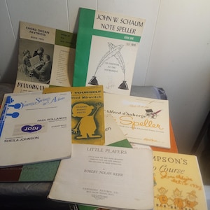 Może przedstawiać: Kolekcja starych książek muzycznych, w tym tytuły takie jak "Chord Organ Favorites", "John W. Schaum Note Speller" i "Little Players". Książki mają kolorowe okładki i ilustracje, prezentujące różnorodne materiały edukacyjne muzyczne.