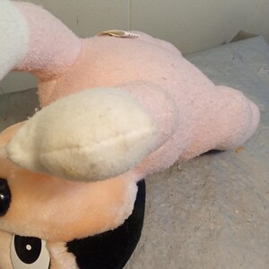 May include: A vintage plush toy featuring a pink body, cream-colored accents, and black details. The toy has a round face with large, expressive eyes and a black and white design. The plush is slightly worn, suggesting it is a well-loved item.