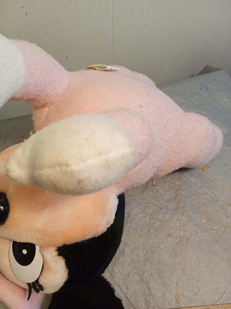 May include: A vintage plush toy featuring a pink body, cream-colored accents, and black details. The toy has a round face with large, expressive eyes and a black and white design. The plush is slightly worn, suggesting it is a well-loved item.
