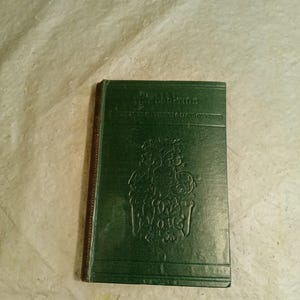 May include: A vintage green book titled "The Dead-Tide" with embossed floral designs. The book's cover is a deep green, with the title and author's name printed in gold lettering. The edges of the book are brown.