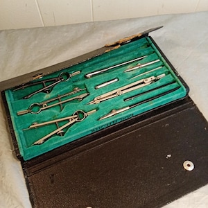 May include: A vintage drafting set in a black leather case. The case is open, revealing a green velvet interior with various silver and black drawing tools. The tools include compasses, dividers, and other precision instruments. The case is slightly worn.