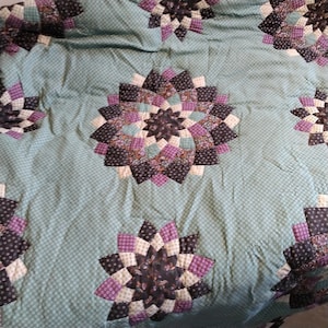 Peut inclure: Une courtepointe bleu sarcelle avec un motif répété de motifs de moulinets violets, blancs et noirs.