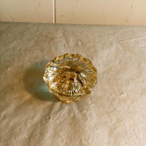 May include: A clear, faceted glass doorknob with a golden hue. The knob has a round shape with a decorative, textured surface. The doorknob is likely vintage and adds a touch of elegance to any door.