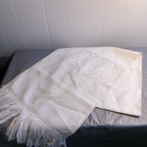 May include: White embroidered fabric with a fringe border. The fabric has a delicate floral pattern and is perfect for a variety of crafting projects.