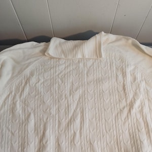 Puede incluir: Un suéter blanco de cuello alto con un patrón de punto de cable.