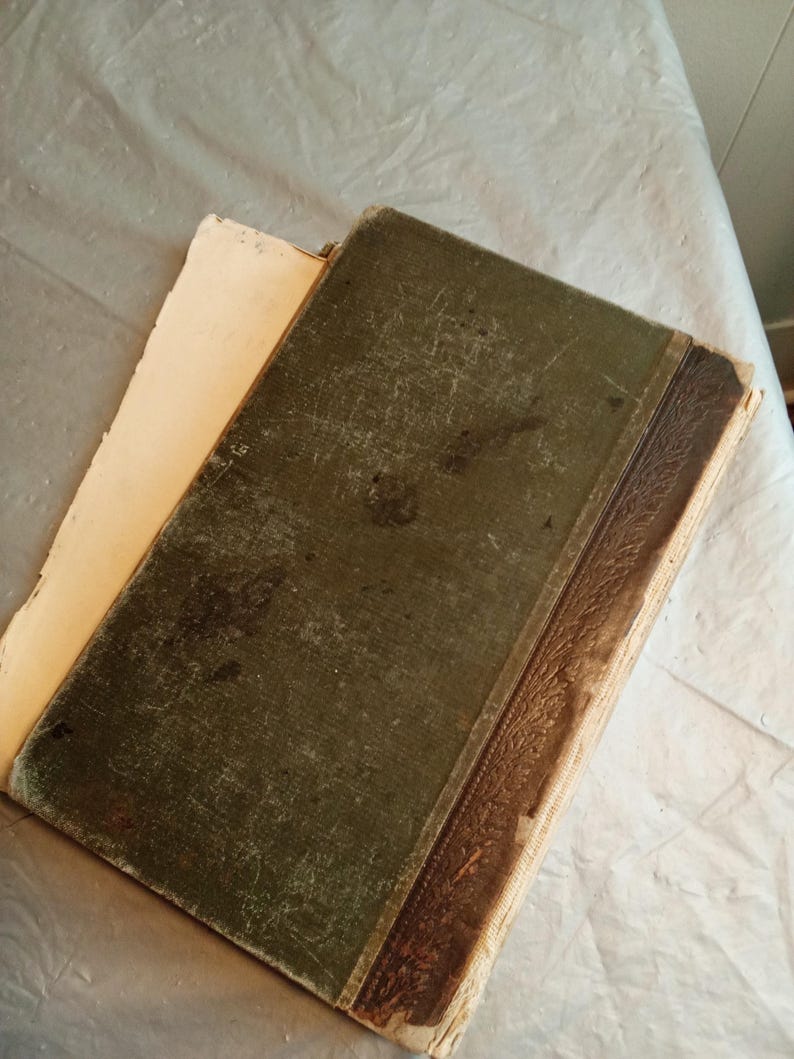 May include: An antique book with a worn, dark green cover and a brown spine. The pages are yellowed with age, and the cover shows signs of wear and tear. The book is open, revealing the aged pages.
